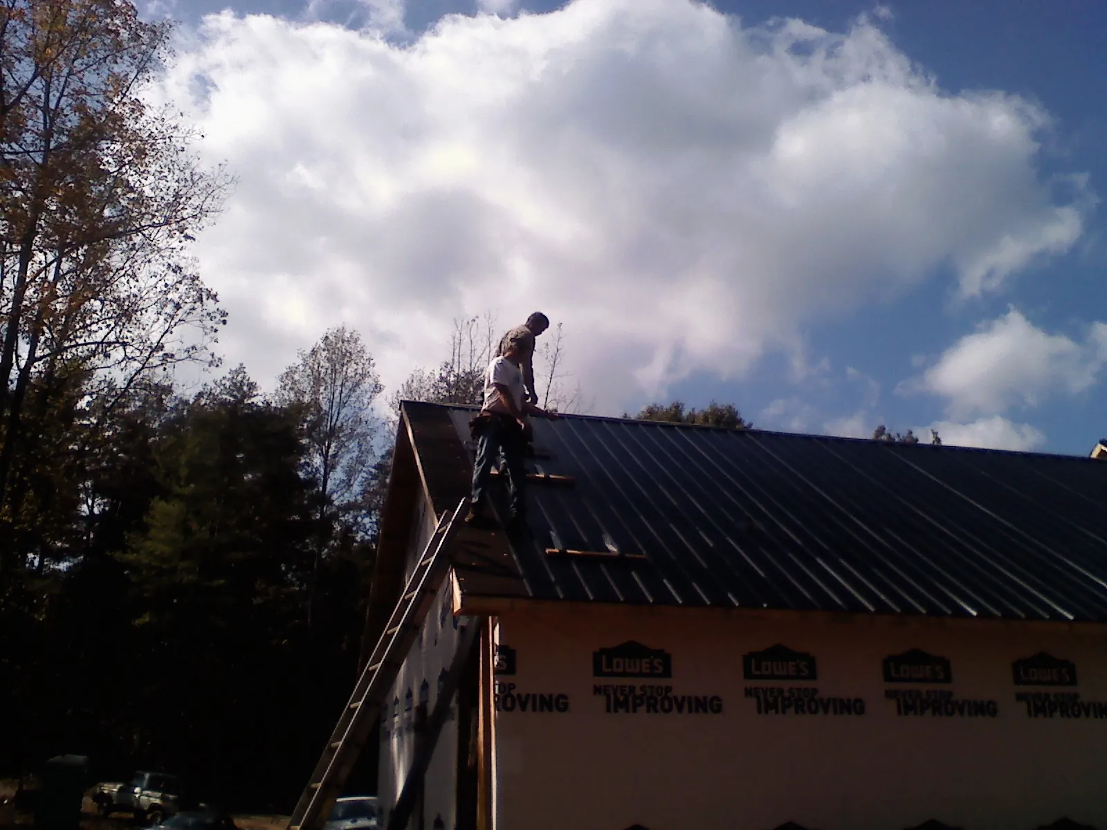 Roofer fastening dark metal panels high against a cloudy sky, from a Roof Inspection job in Pomona